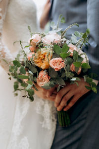 Midsection of bride and groom holding bunch of flowers