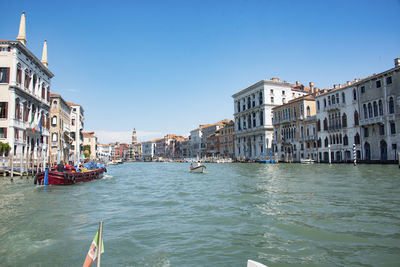 Boats in canal amidst buildings in city against clear sky