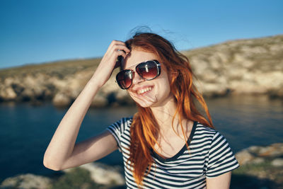 Portrait of smiling young woman wearing sunglasses against sea