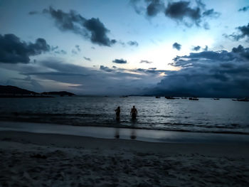 Silhouette people on beach against sky during sunset