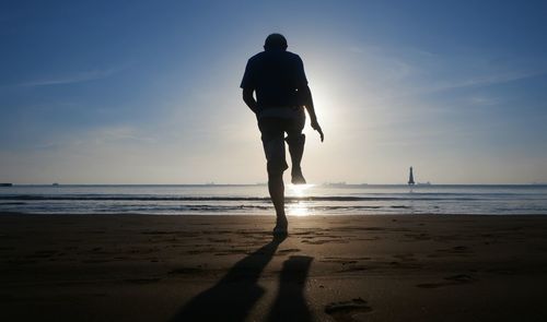 Rear view of silhouette man standing on one leg at beach