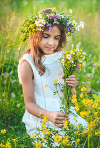 Girl wearing floral crown holding flowers in meadow