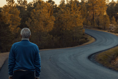 Rear view of senior man standing on road during autumn
