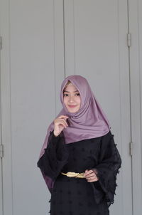 Portrait of smiling young woman standing against wall