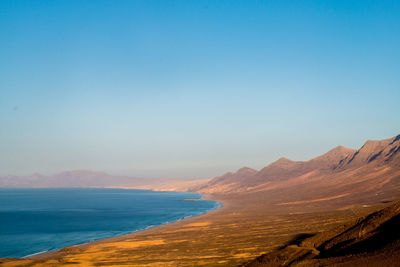 Scenic view of sea and mountains against clear blue sky