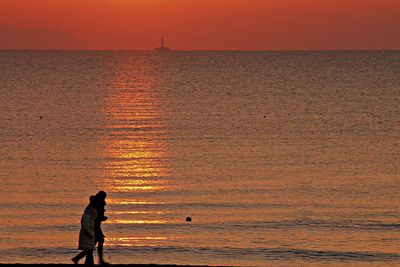 Silhouette woman standing on beach against orange sky