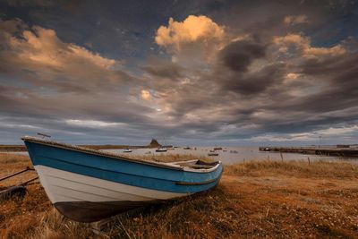 Boat moored on beach against sky during sunset