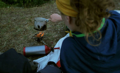 Female hiker making drink while leaning on bed at field during camping