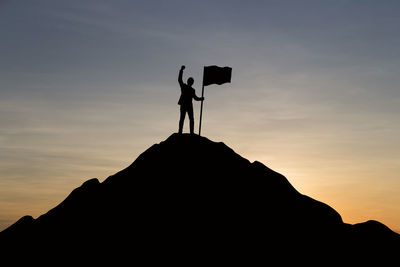 Silhouette man standing on rock against sky during sunset