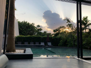 Swimming pool by trees against sky during sunset