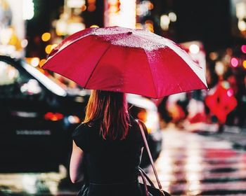 Rear view of woman with umbrella on street during rainy season