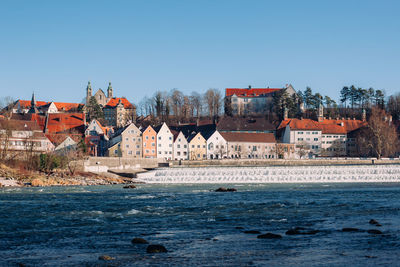 Buildings by river against clear blue sky