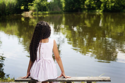 Rear view of girl sitting by lake