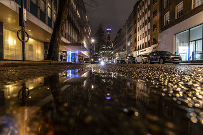 Reflection of illuminated buildings in puddle on street