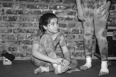 Cute girl sitting by friend on floor against brick wall