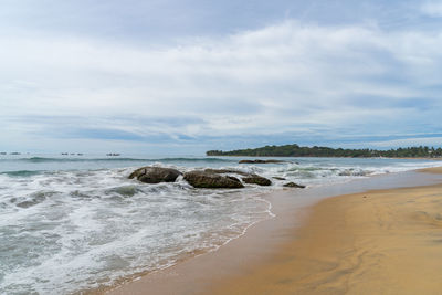 Tropical beach with rocks in the sea. palm trees on the background. cloudy sky