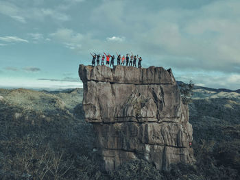 Friends posing while standing on cliff against sky