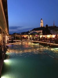 Illuminated buildings by river against sky at night