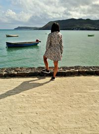 Rear view of woman standing by sea against sky