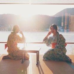 Young women wearing kimonos sitting by window 