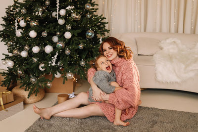 Happy mom and little daughter kid in sweaters hugging getting ready for  christmas holiday at home