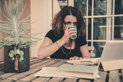 Woman drinking coffee while reading book on table