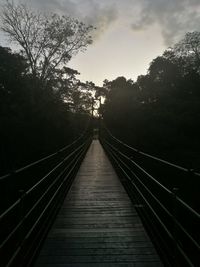 Bridge leading towards trees against sky