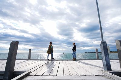 Friends standing on wood by sea against sky