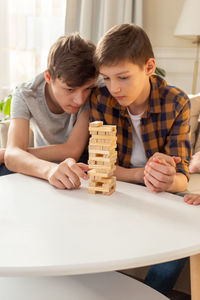 A two teen boys are enthusiastically playing a board game made of wooden rectangular blocks