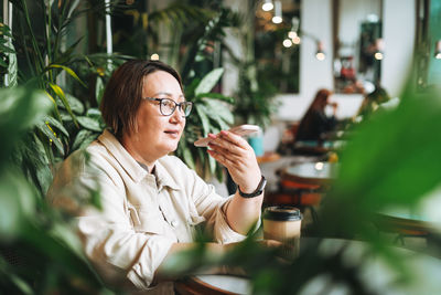 Adult middle aged woman plus size in casual clothes with coffee using mobile phone in cafe