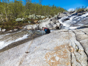 Low angle view of woman drinking water from stream flowing through rocky hill