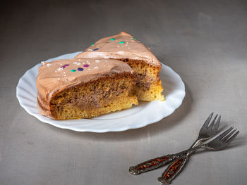 Two servings of homemade cream cake on a white plate and dessert forks on a gray background