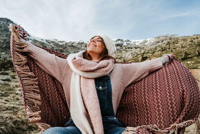 Woman wearing knit hat sitting in footpath against field