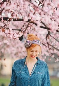 Portrait of smiling young woman with pink cherry blossom on tree