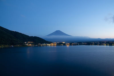 View of illuminated city by lake against blue sky at night