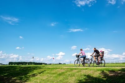 People riding bicycle on field against sky