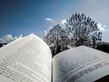 Close-up of open book on plant against sky