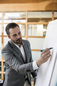 Mid adult businessman writing on flip chart during presentation in office