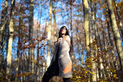Low angle view of woman standing amidst trees in forest