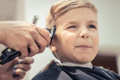 Cropped hands of female hairdresser styling boy hair in salon