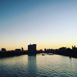 Silhouette buildings by river against sky during sunset