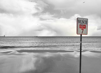 Warning sign on sea shore against cloudy sky