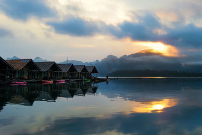 Scenic view of houses by lake against cloudy sky at dusk