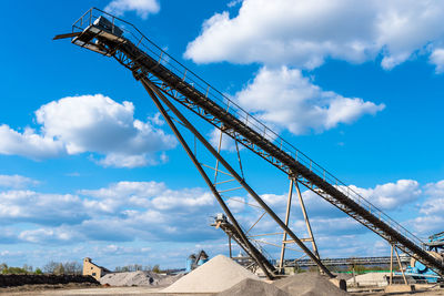 Conveyor over heaps of gravel on blue sky at an industrial cement plant.