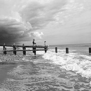 People on pier at sea against sky