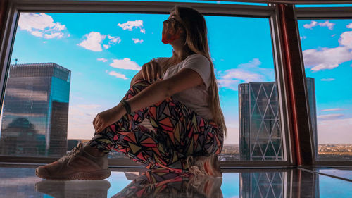 Woman standing by window against sky