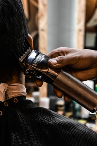 Cropped hand of barber cutting male customer hair in shop