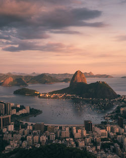 Aerial view of buildings in city by sea against cloudy sky during sunset