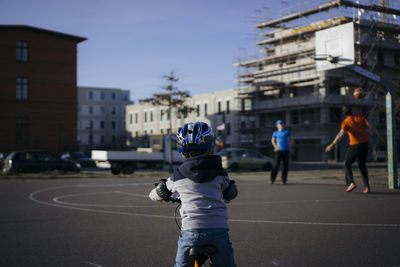 Rear view of boy on bicycle looking at men playing basketball