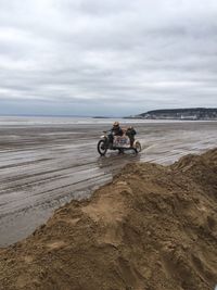 Man with friend riding motorcycle on beach against sky